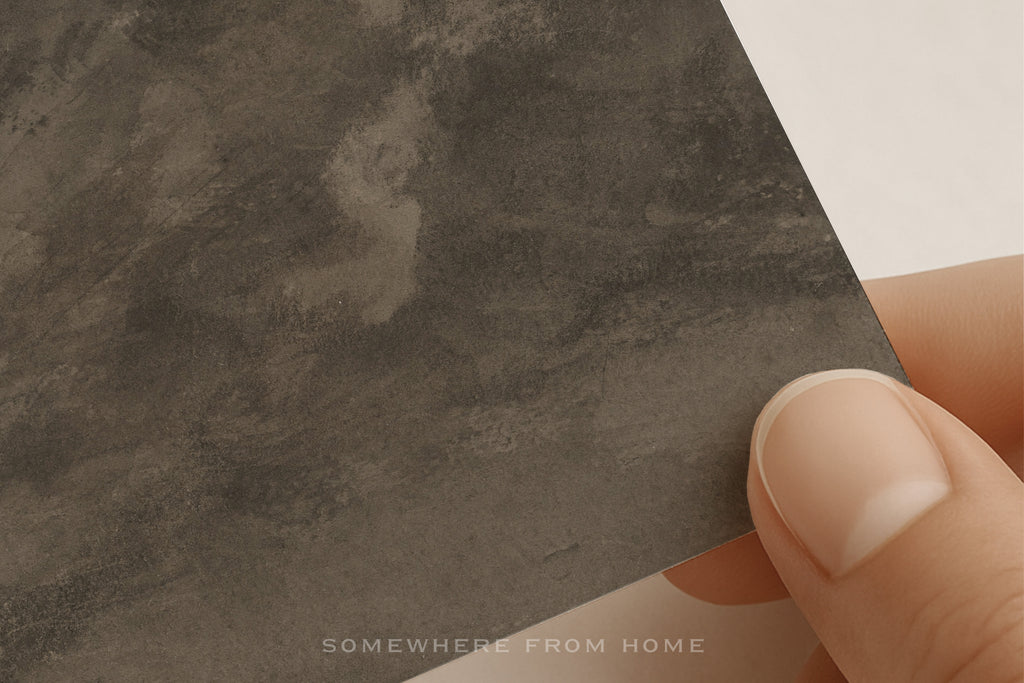 A close-up of a hand holding a square sample of a muted landscape mountain paper art print on textured paper