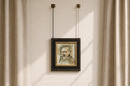 A framed portrait painting of a man with a mustache, hanging from two chains on a beige wall between beige curtains.