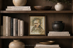 A framed portrait painting of Albert Einstein displayed on a dark wooden shelf, surrounded by books, ceramic vases, and bowls in a cozy, styled interior setting.
