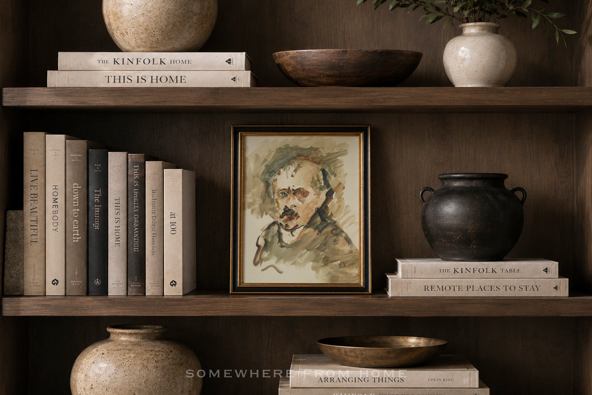 A framed portrait painting of Albert Einstein displayed on a dark wooden shelf, surrounded by books, ceramic vases, and bowls in a cozy, styled interior setting.