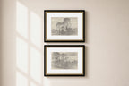 Two framed landscape art prints with black frames and gold inner trim, displayed vertically on a beige wall with soft window shadow light.