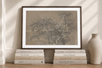 A framed art print featuring a detailed, textured botanical illustration of a tree, styled on a wooden floor with decorative books and a ceramic vase against a cream-colored wall.