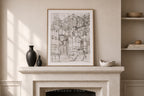 A framed black and white architectural sketch print hangs on a beige wall above a stone fireplace mantel styled with dark vases and a small bowl.