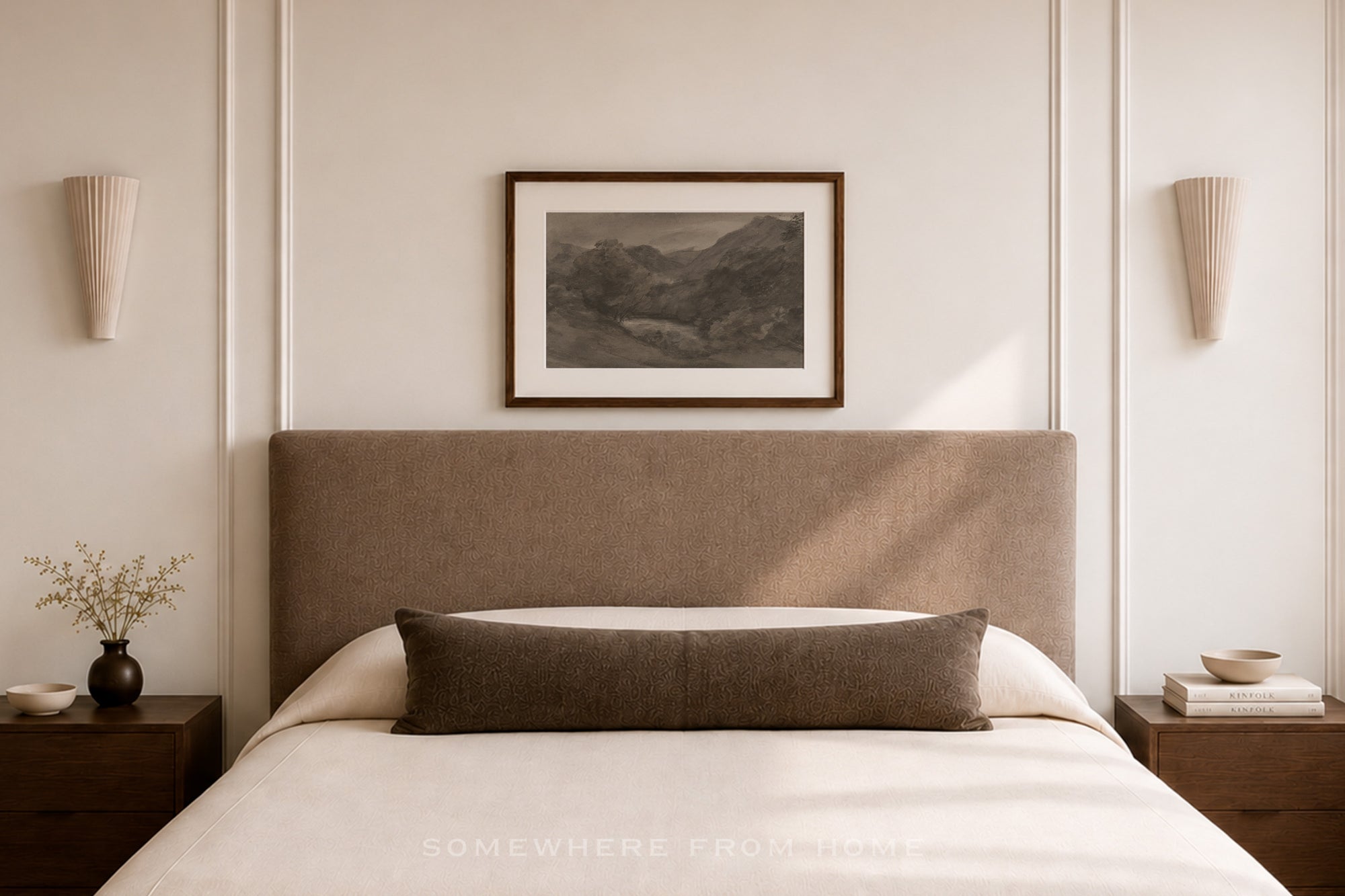 A styled bedroom scene featuring a bed with a tall upholstered headboard, white bedding, a dark brown lumbar pillow, matching bedside tables and sconces, and a framed landscape print on the wall.