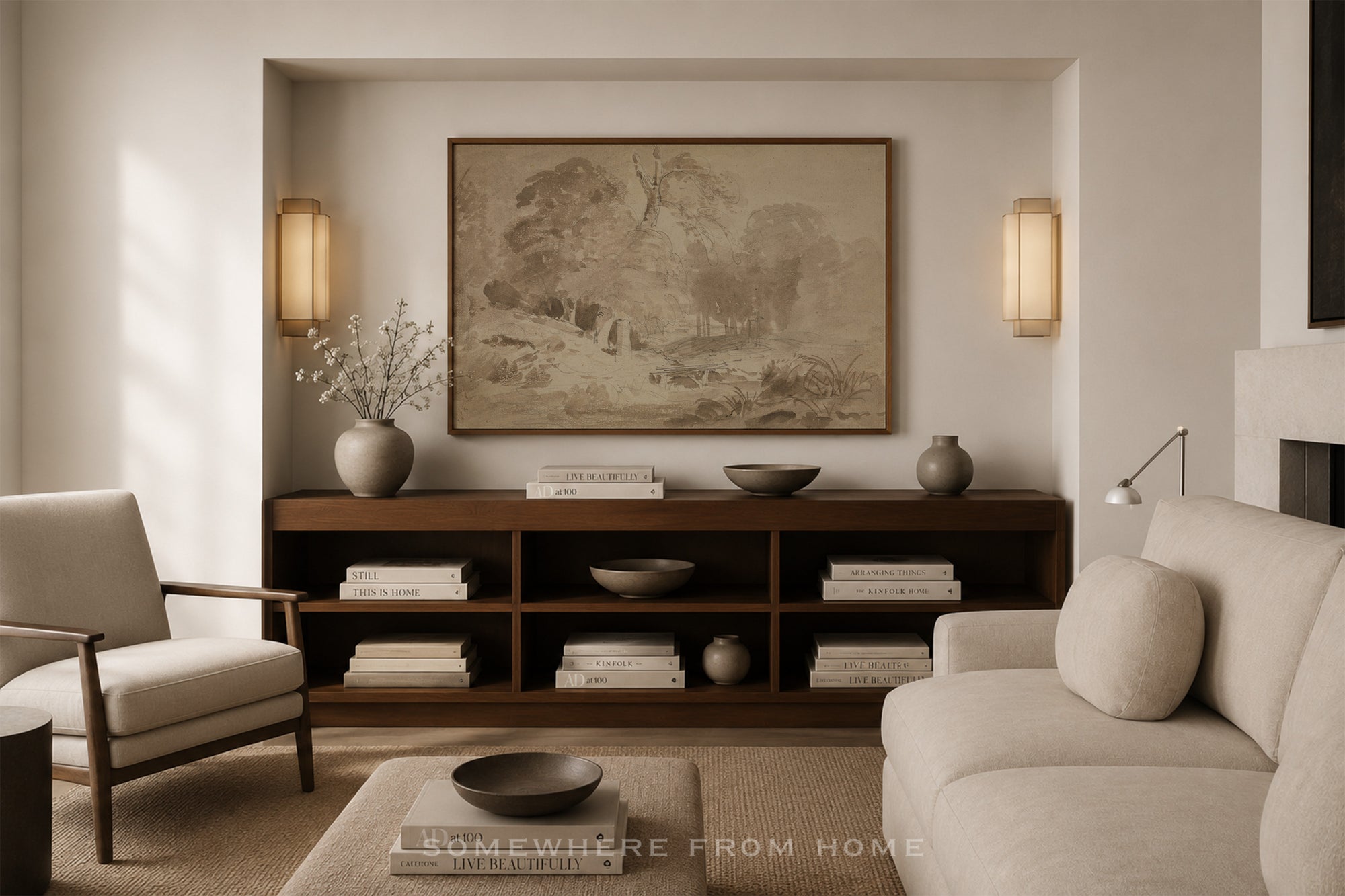 A styled living room interior featuring a large framed landscape painting on a beige wall above a dark wood console. The room includes a light beige sofa, a matching armchair, a coffee table, and decorative ceramic vases and books.