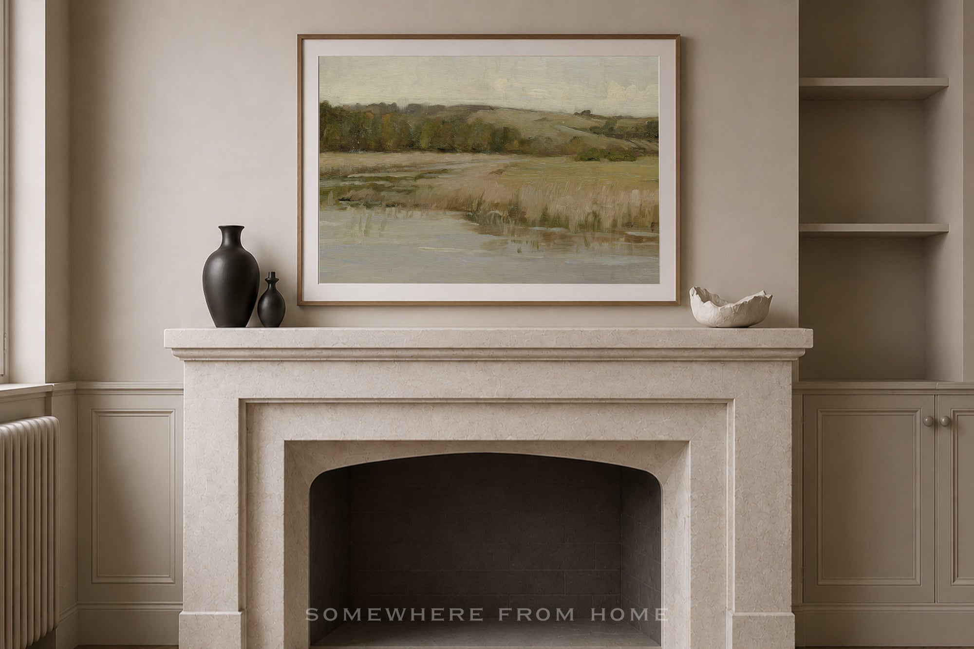 A framed landscape painting of a marshy field and river is displayed on a light stone fireplace mantel in a neutral beige room, flanked by two dark vases and a small white bowl.